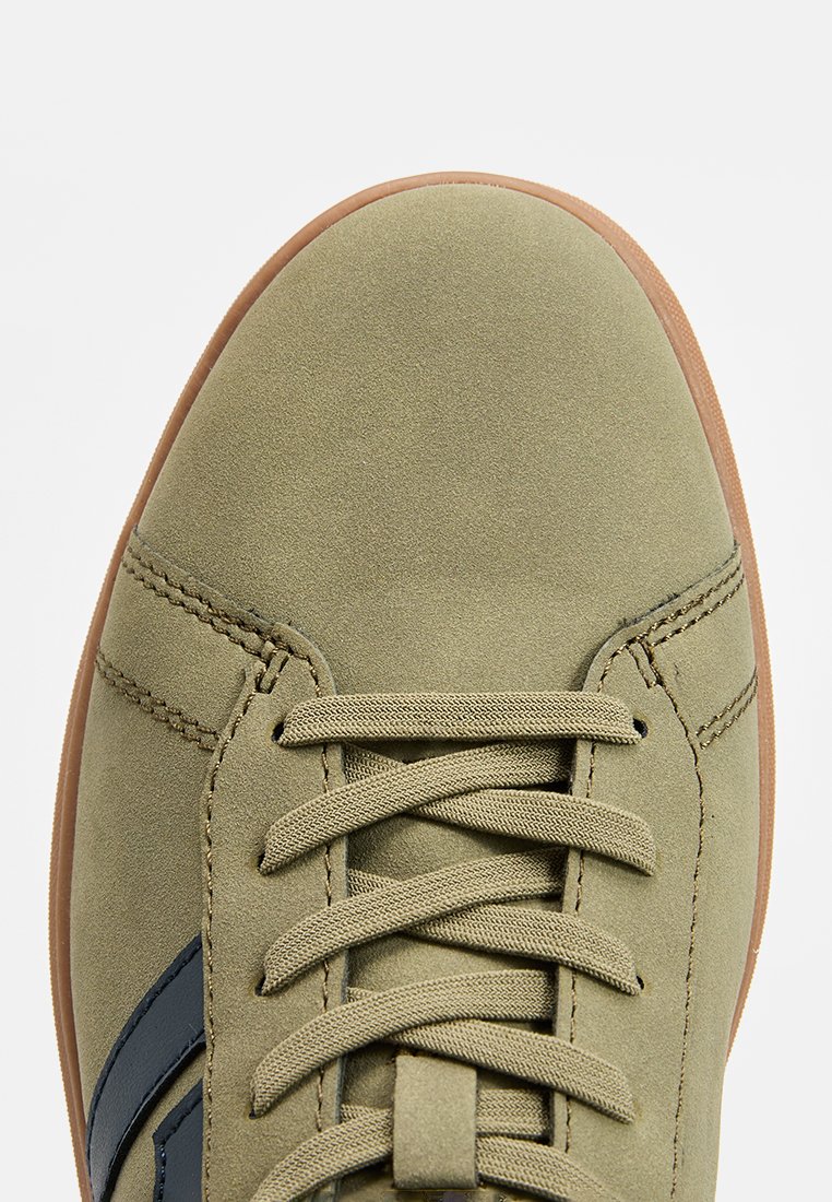 Nahaufnahme eines olivgrünen Wildledersneakers mit beigen Schnürsenkeln und brauner Gummisohle, ausgestattet mit einem dunkelblauen Streifen an der Seite.