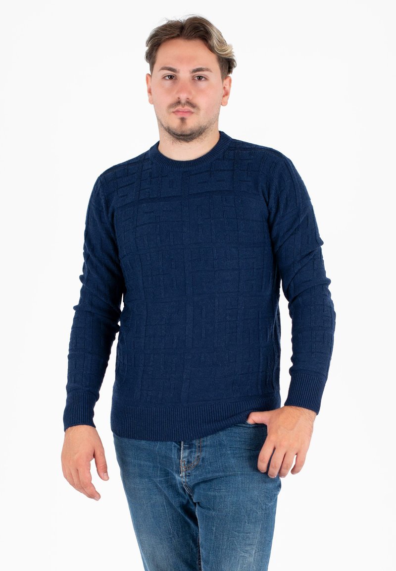 Granatowy sweter dziewiarski z teksturowanym geometrycznym wzorem, okrągłym dekoltem oraz prążkowanymi mankietami i dolnym wykończeniem, zestawiony z niebieskimi dżinsami.