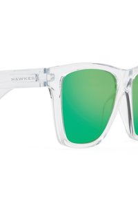 Klare Kunststoffsonnenbrille mit grünen Verlaufsgläsern. Quadratische Form, mit dem Markennamen "HAWKERS" am Bügel. Einfaches Design mit sichtbaren Scharnieren.