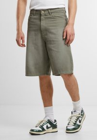 Shorts in denim verde oliva caratterizzati da un taglio dritto, vita standard con chiusura a bottone e tasche laterali. Abbinati a sneakers.