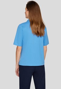 Helles Blau Kurzarm-Polohemd mit klassischem Kragen, aus glattem Stoff gefertigt. Seitliche Schlitze am Saum für Bewegungsfreiheit.