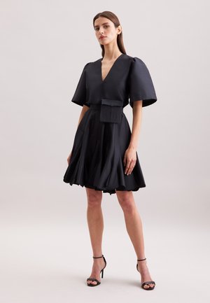 Schwarzes Kleid mit tiefem V-Ausschnitt, Puffärmeln und einem ausgestellt geschnittenen Rock. Verfügt über eine Vordertasche. Glatter, strukturierter Stoff mit einem formellen Design.