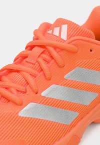 Φωτεινό πορτοκαλί αθλητικό παπούτσι με υφασμάτινη υφή, πορτοκαλί κορδόνια και τρεις ασημένιες ρίγες στο πλάι.