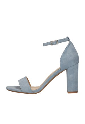 Lyseblå ruskindssandal med høj hæl, anklestrop og spænde, åben tå og blokhæl på hvid baggrund.