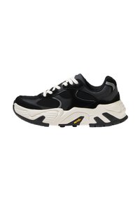 Fekete sportcipő fehér fűzőkkel, szintetikus anyagból készült. Texturált fekete panelek, vastag fehér középtalpal és fekete gumitalp jellemzi.