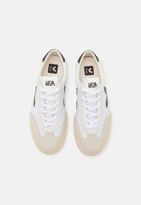 Fehér és krémszínű sneakers, texturált velúr orral, kontrasztos fekete részletekkel, lapos fűzőkkel és logóval ellátott nyelvvel. Kerek orrú kialakítással rendelkezik.