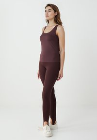 Canottiera sportiva bordeaux abbinata a leggings coordinati, con un design aderente, texture liscia e aperture alla caviglia. Sneakers bianche completano il look.