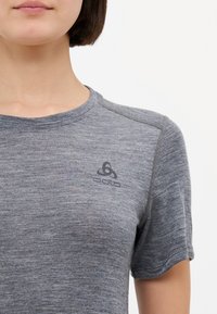 T-shirt gris à manches courtes fabriqué dans un matériau texturé, avec un col rond et un petit logo noir sur la poitrine.