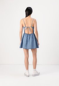 Denim skater obleka z nastavljivimi naramnicami, odprtim hrbtom in nabranim krilom. Obuta z belimi supergami.