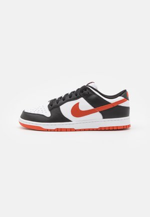 Black and white sneaker with an orange Nike logo. Features a textured leather upper and a rubber sole with contrasting orange accents.