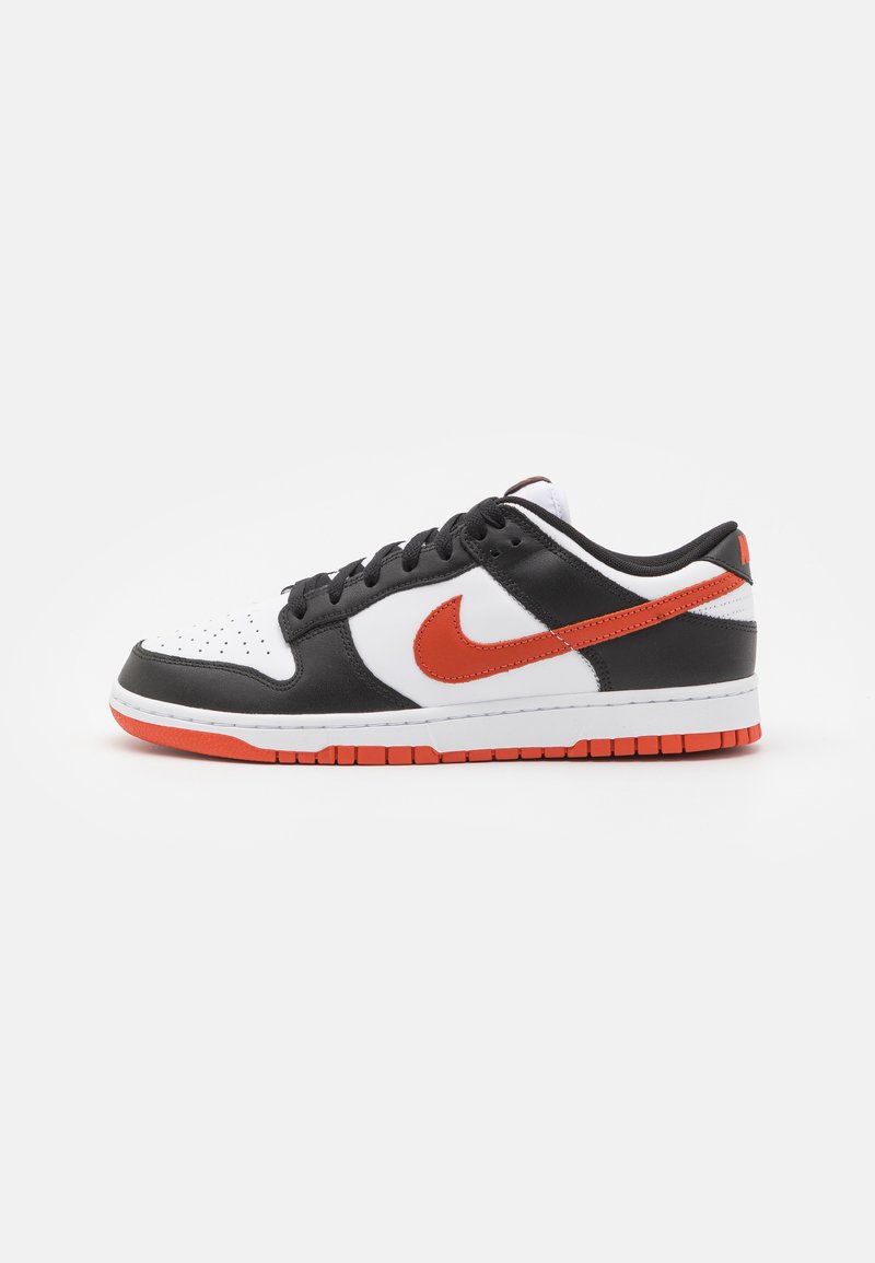Baskets noir et blanc avec un logo Nike orange. Elles présentent une tige en cuir texturé et une semelle en caoutchouc avec des accents orange contrastants.