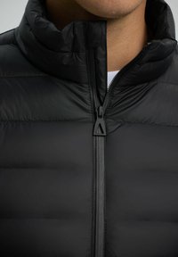 Black puffer jacket featuring a high collar and zip closure. The fabric appears smooth with visible quilted sections and a matte finish.
