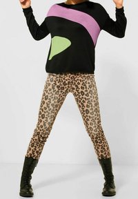 Svart tröja med abstrakta mönster i lila och grönt, kombinerad med leopardmönstrade skinnyjeans och svarta snörade kängor.