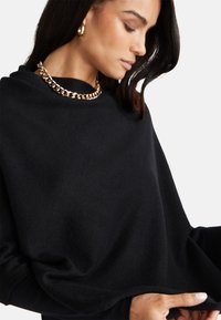 Černý pletený top s volným střihem, dlouhými rukávy a ribkovaným výstřihem. Ozdobený chunky zlatým řetízkem.
