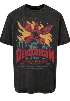 T-shirt oversized noir avec un design graphique coloré d'un Demogorgon, éléments de texte en rouge et bleu, texture usée et col rond.