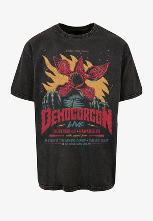 Schwarzes übergroßes T-Shirt mit einem bunten Grafikdesign eines Demogorgons, ergänzt durch Textelemente in Rot und Blau, mit einem verwitterten Textur und Rundhalsausschnitt.