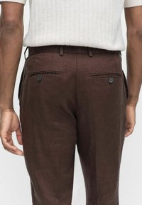 Bruna linbyxor med två bakfickor, var och en prydd med en blå knapp. Tyget har en mjuk struktur och en avslappnad passform.