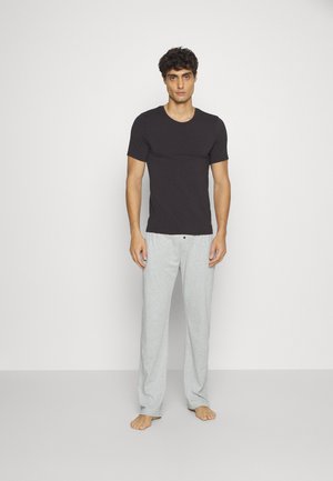 Zwart T-shirt met korte mouwen, gecombineerd met lichtgrijze loungebroek, met een relaxte pasvorm en zachte stof, blootsvoets gedragen.