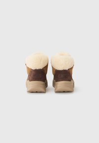 Botas de tobillo de ante marrón con forro de piel de oveja crema, suelas de goma beige y un detalle de logo cosido en la parte trasera. Textura suave y diseño duradero.