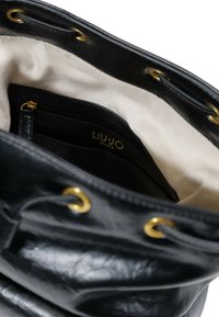 Borsa a secchiello nera in pelle con hardware dorato, dotata di fodera interna beige, tasche interne e chiusura a laccio.