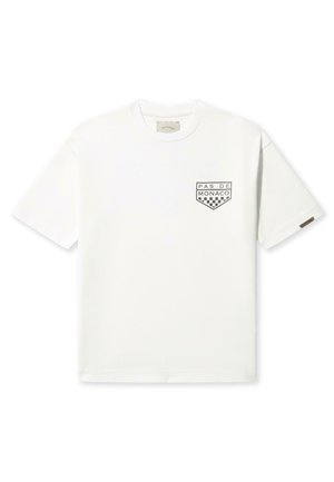 White cotton t-shirt featuring a small black graphic with "PAS DE MONACO" and a checkerboard pattern on the left chest. Classic fit.