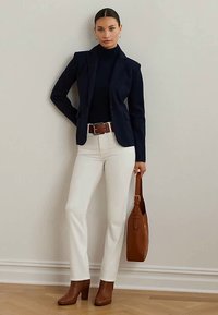 Blazer azul-marinho sobre um pulôver de gola alta azul-marinho, calças creme, cinto castanho, botas de salto alto castanhas e uma mala de ombro castanha. Texturas suaves, ajuste sob medida.