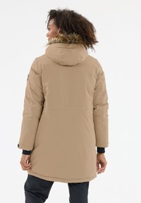 Beige, pehmustettu parka, jossa on turkisreunainen huppu, pitkät hihat ja helma, joka ulottuu polvien ylle. Ominaisuuksina yksinkertainen ja virtaviivainen muotoilu.