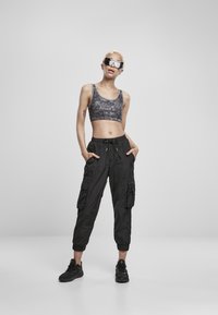 Grijze camouflage crop top gecombineerd met zwarte cargo broek met zijzakken en elastische cuffs. Zwarte sneakers maken de outfit compleet.