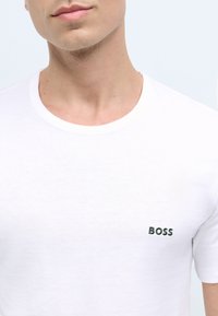 White cotton t-shirt featuring a round neckline and a subtle green embroidered "BOSS" logo on the left chest. Smooth texture.