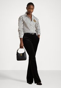 Cămașă cu dungi albe și negre, cu un logo brodat în aur. Pantaloni flared din catifea neagră și o geantă mică neagră cu detalii aurii.