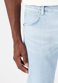 Světle modré džíny se slim fit střihem, s předními kapsami a kovovým knoflíkem. Látka má hladkou texturu.