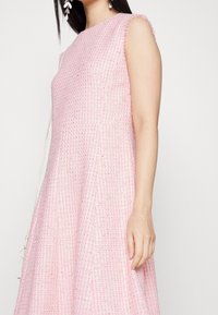 Vaaleanpunainen teksturoitu mekko, jossa on istuva päälliosa ja levenevä hame, lyhyillä hihoilla ja hienovaraisella kudontakuviolla.