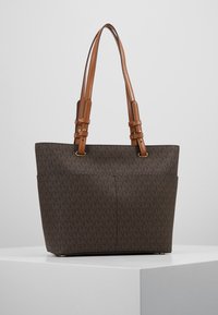 Sac fourre-tout marron avec motif monogramme foncé, deux bretelles réglables en cuir beige, forme rectangulaire, et fond plat.