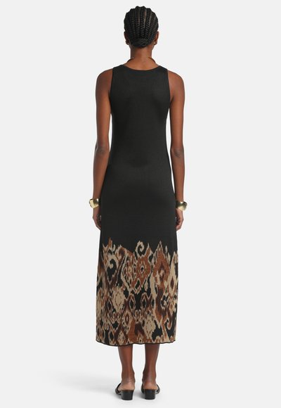 Žena s pletenými vlasmi nosí čierne midi šaty bez rukávov s hnedými a béžovými abstraktnými vzormi na leme, čierne sandále na podpätku a zlaté náramky.