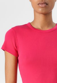 T-shirt en maille près du corps de couleur rose vif, avec un col rond et des manches courtes, fabriqué en tissu doux extensible avec une finition texturée.