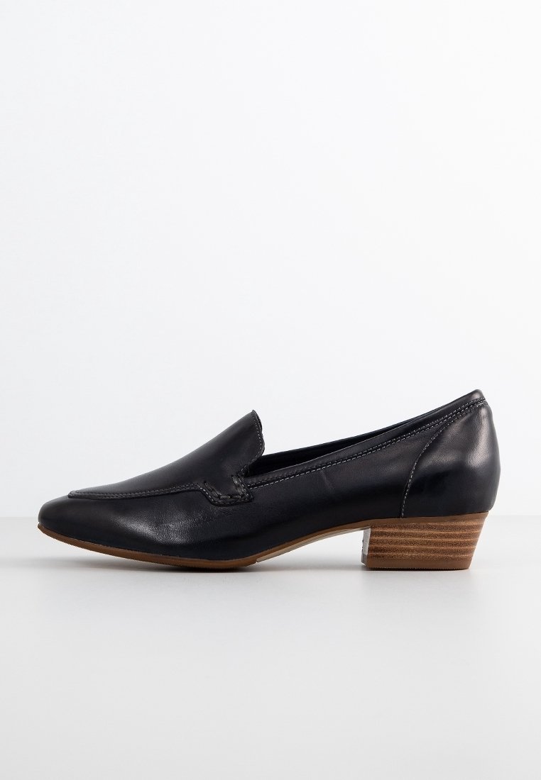Chaussure slip-on en cuir noir avec un faible talon empilé, un bout pointu et des coutures décoratives sur le dessus. Texture lisse et design minimaliste.