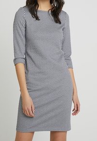 Šedobílý vzorovaný šat s tříčtvrtečními rukávy, rovný střih a kulatým výstřihem. Obsahuje texturovanou látku.