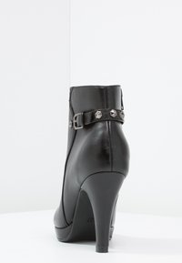Schwarze Lederstiefelette mit hohem Stiletto-Absatz, ausgestattet mit einem seitlichen Riemen mit Schnalle und Pyramidennieten sowie einer glatten Oberfläche.
