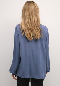 Blå langærmet bluse med løst fit, lavet af svævende stof, med subtil tekstur, manchetter ved ærmerne og en buet nederste kant.