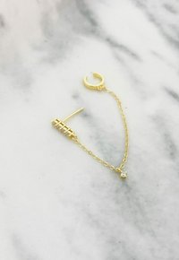 Orecchino a cerchio in oro con una sottile catena, un ciondolo rettangolare e un piccolo zirconia cubico all'estremità. Texture liscia, finitura luminosa.