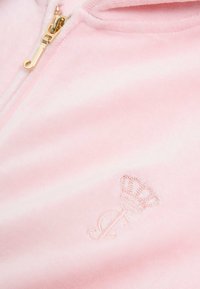 Roze capuchonvest met ritssluiting gemaakt van zacht stof, voorzien van een gouden ritssluiting en een subtiele geborduurde kroon en initialen in lichtroze.