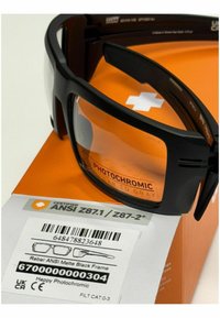 Okulary fotochromowe z matową czarną oprawką, pomarańczowymi soczewkami i certyfikatem ANSI, wyeksponowane na pomarańczowym pudełku z etykietami i kodami kreskowymi.