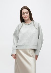 Sweatshirt cinzenta com detalhes em pedraria no decote, com corte descontraído e mangas compridas, combinada com uma saia bege de tecido sedoso.