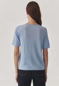 Tricou scurt cu mânecă, de culoare albastră, dintr-un material moale, cu decolteu rotund. Prezintă cusături vizibile de-a lungul marginilor și o croială lejeră.