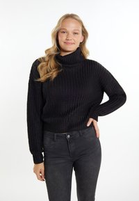 Schwarzer gerippter Strickpullover mit hohem Rollkragen und langen �Ärmeln, kombiniert mit dunkelgrauen eng anliegenden Jeans. Glatte Textur, lässiges Design.