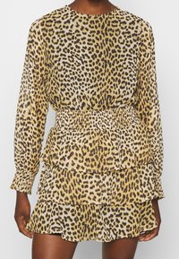 Mekko, jossa on jaguaari-kuosi, pitkät hihat, rypistetty vyötärö ja kerrokselliset röyhelöt. Valmistettu kevyestä kankaasta vaaleanruskeassa, mustassa ja kermanvärisessä sävyssä.