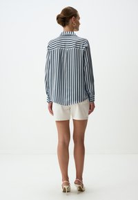 Gestreept blouse in blauw en wit, lange mouwen, knoop manchet, achterdeel met plooi, gecombineerd met witte shorts en sandaaltjes met bandjes.