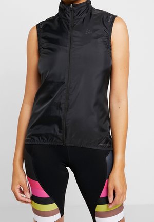 Veste noire sans manches zippée portée avec un short de cyclisme noir présentant des bandes horizontales roses, jaunes, marron et blanches près des genoux.