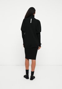 Μαύρο φόρεμα με ψηλό γιακά, ραβδωτή υφή και εφαρμοστό φούστα. Διαθέτει φουσκωτά μανίκια και μια μικρή ετικέτα στον πίσω λαιμό.