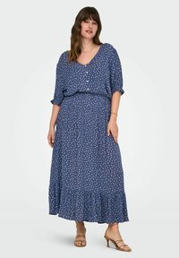 Tumši zili maksi kleita, kas izgatavota no viegla auduma, ar V veida kaklu, īsām piedurknēm, baltām punktiņām un viļņotu apakšmalu.